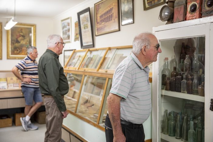 Two visitors looking into cabinets of bottles and framed pictures