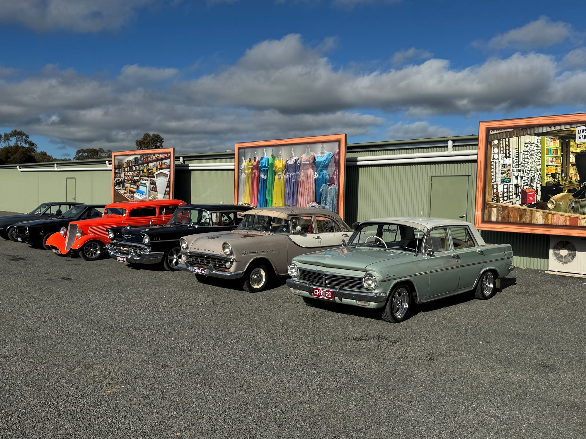 Classic cars parked outside the museum, below large display panels showing the shops, the gown collection and the garage