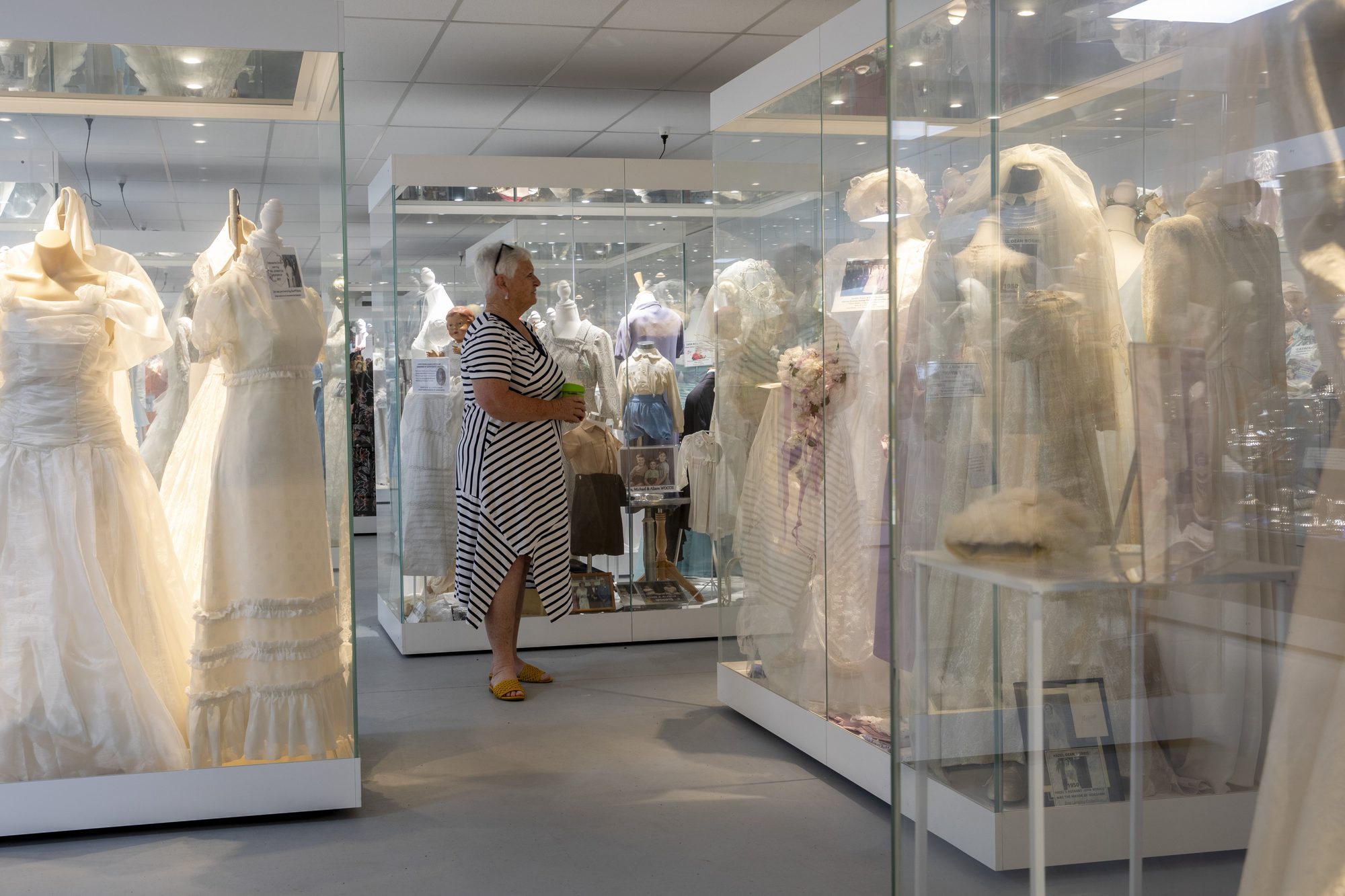 A visitor walking between lit glass cases of wedding gowns and period clothing