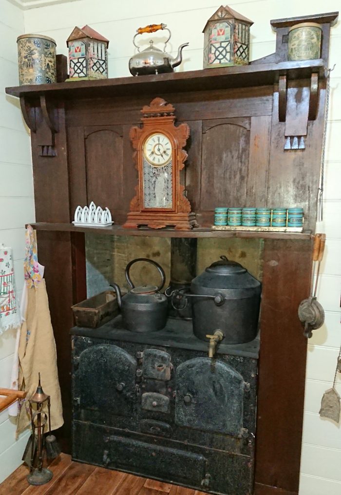 A kitchen dresser set with clocks, jugs and enamelware above a wood stove