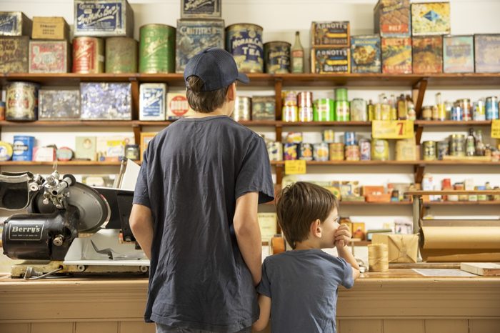 A man and a boy at the grocery counter, backed by a wall of tins