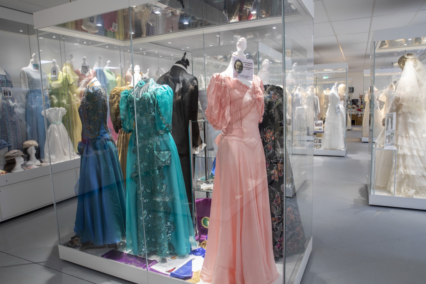 Colourful wedding and ball gowns in glass display cases